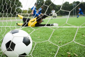 Soccer, view through net of players scoring goal, soccer ball in foreground